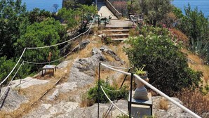 Una torre de piedra con una escalera que lleva a una puerta, rodeada de vegetación y con vistas a un cuerpo de agua.