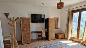 Una habitación con cama, escritorio, silla, televisor y balcón con cortinas.