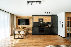 Une cuisine moderne avec une table et des chaises en bois, un téléviseur à écran plat fixé au mur et un four encastré.