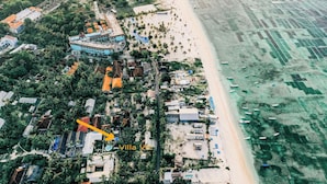 An aerial view of Villa Vie, featuring a beachfront property with multiple buildings, a swimming pool, and a beach area with umbrellas. - Villa Vie (Lembongan Island)