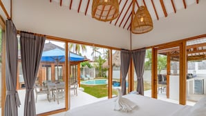 A spacious bedroom with a large bed, a view of a swimming pool, and a patio area with outdoor furniture. - Villa Vie (Lembongan Island)