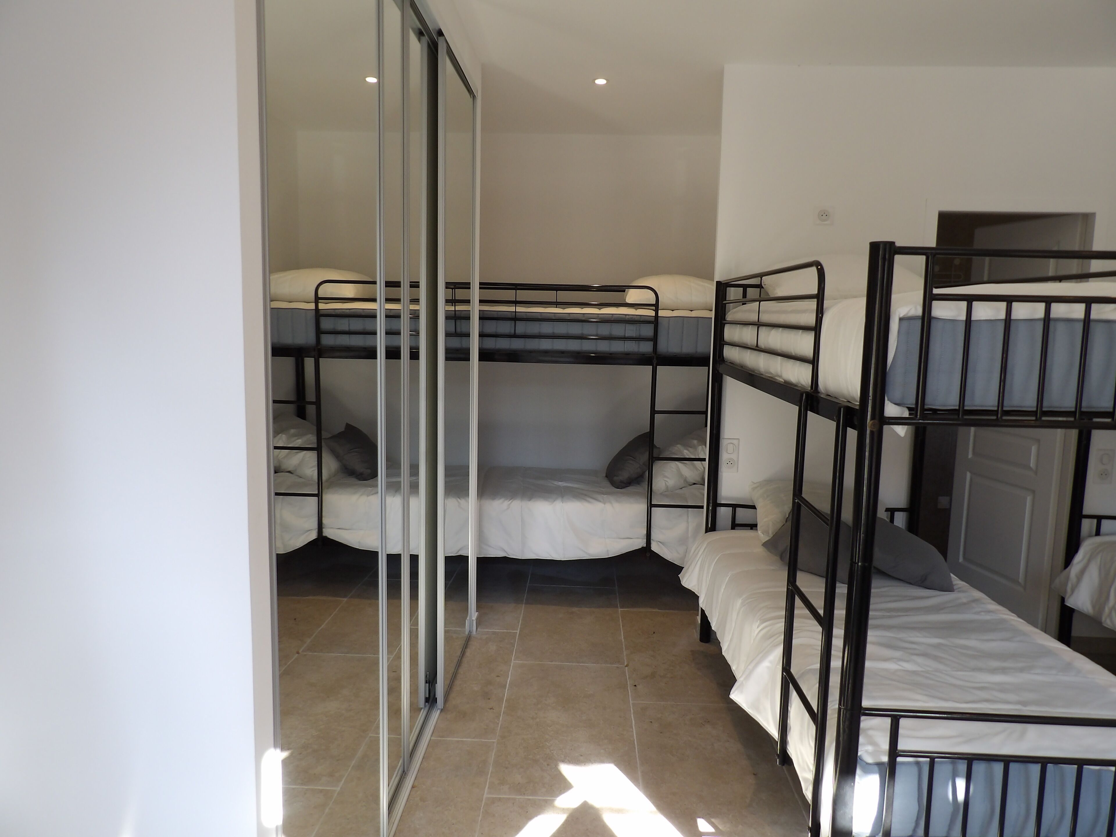 A dormitory room with bunk beds, a sliding door, and tiled flooring.