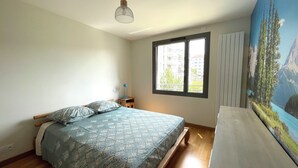 A bedroom with a bed, a window, a desk, and a painting on the wall.