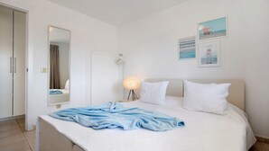 A bedroom with a bed, a bedside lamp, a mirror, and a wall with framed pictures.