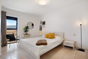 A bedroom with a bed, a nightstand, a chair, a plant, a mirror, and a window with curtains.