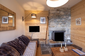 A cozy room with a stone fireplace, wooden walls, a sofa, a television, and a small table with candles.