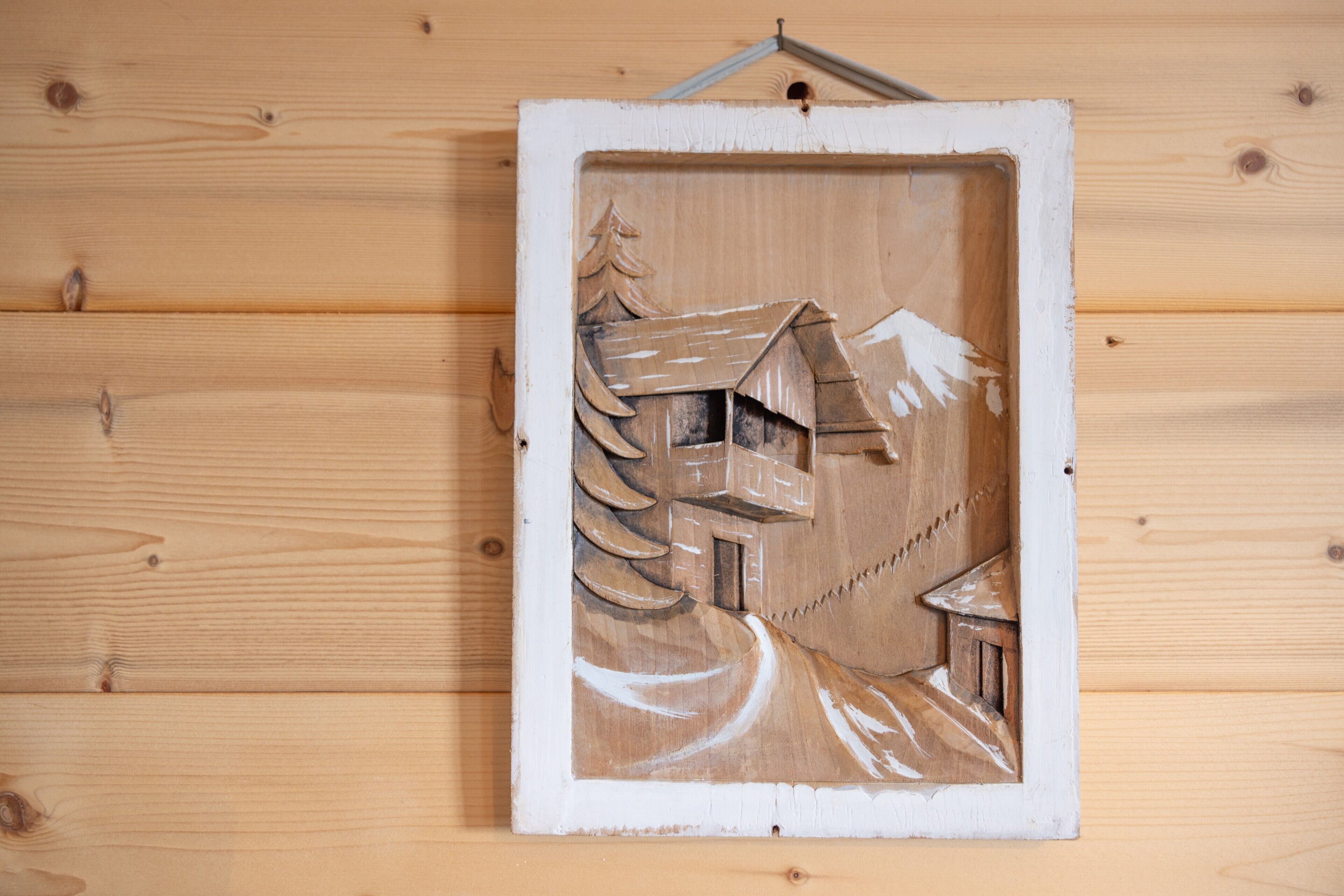 Une sculpture en bois représentant une maison, avec une montagne et des arbres en arrière-plan.