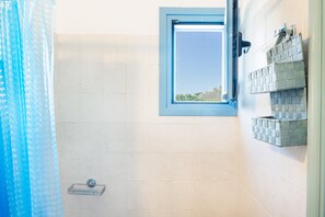 A bathroom with a window, tiled walls, a shower curtain, and a shelf with toiletries. - Holiday Home 'Beachfront Lampis Dolphin 1' with Sea View, Wi-Fi and Air Conditioning (lampi)
