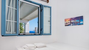 Une pièce avec un lit, une fenêtre avec des rideaux et un tableau au mur.
