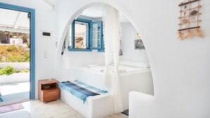 Een slaapkamer met een bed, een klein nachtkastje, een raam met blauwe randen en uitzicht op buiten.