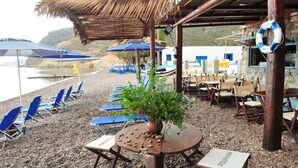 Een zitgedeelte aan het strand met parasols, lounge fauteuils en een tafel met een potplant.