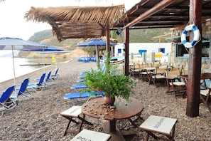 A beachside seating area with umbrellas, lounge chairs, and a table with a potted plant.
