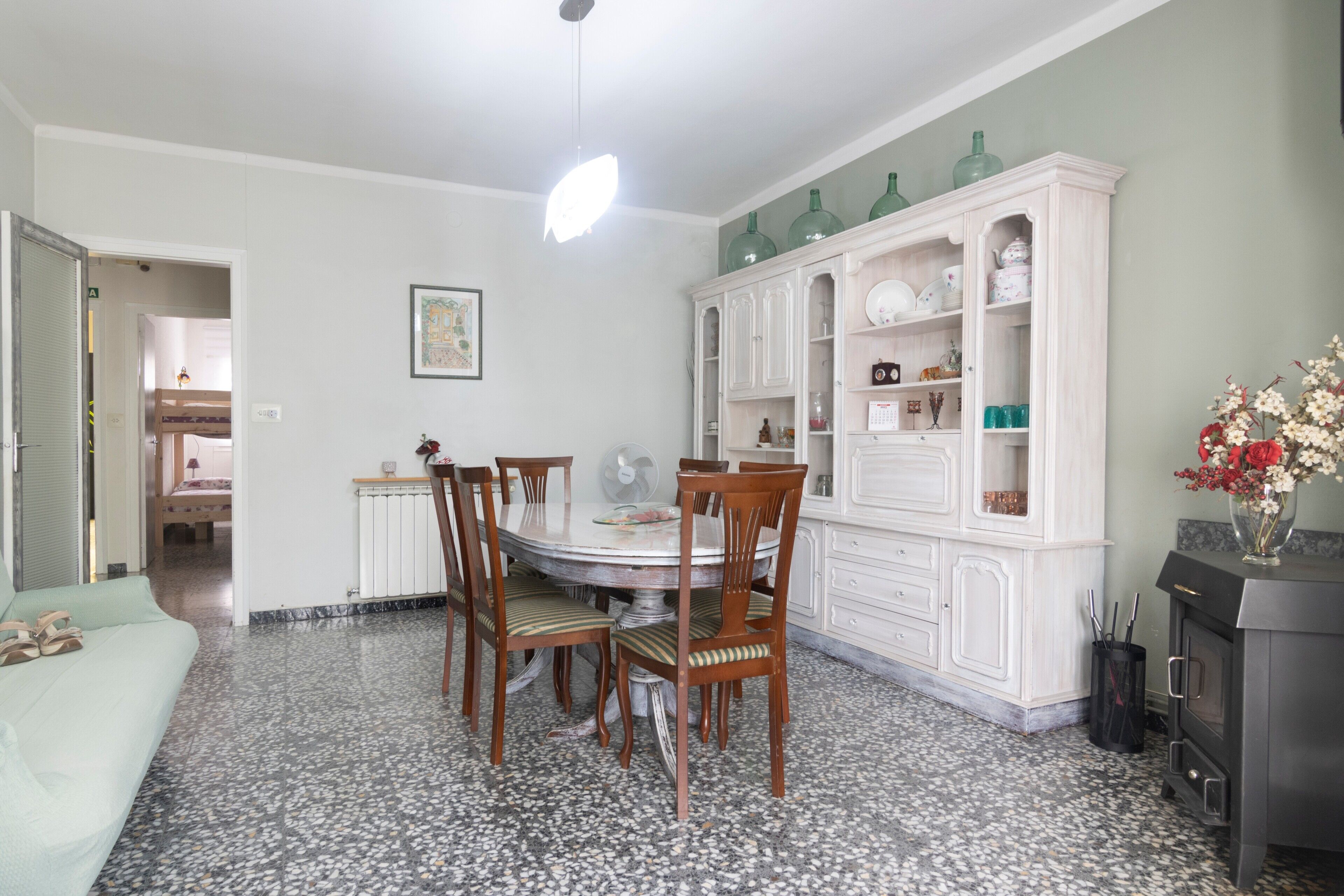 A dining area with a round table, chairs, a white cabinet with glass doors, and a fan.