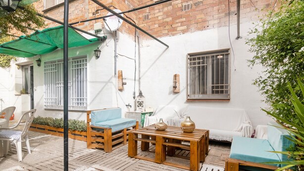 A courtyard with wooden furniture, a green umbrella, and a white wall with windows. - Holiday Home 'Cal Marcos' with Private Terrace, Private Garden and Wi-Fi (Torregrossa)