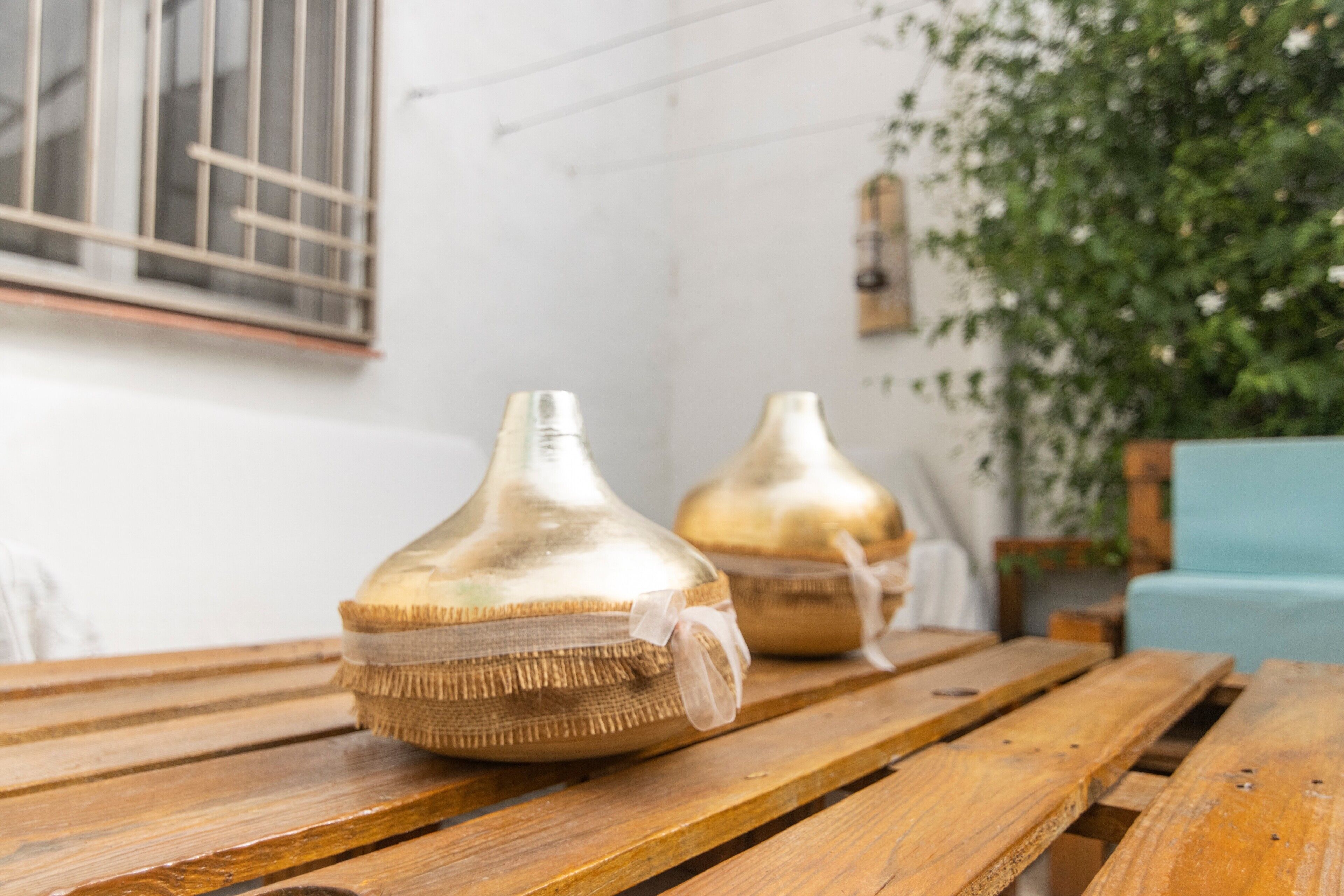 Deux vases dorés sont posés sur une table en bois, avec une fenêtre et une plante en arrière-plan.