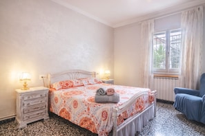 A bedroom with a bed, two bedside lamps, a chair, a dresser, and a window with curtains.