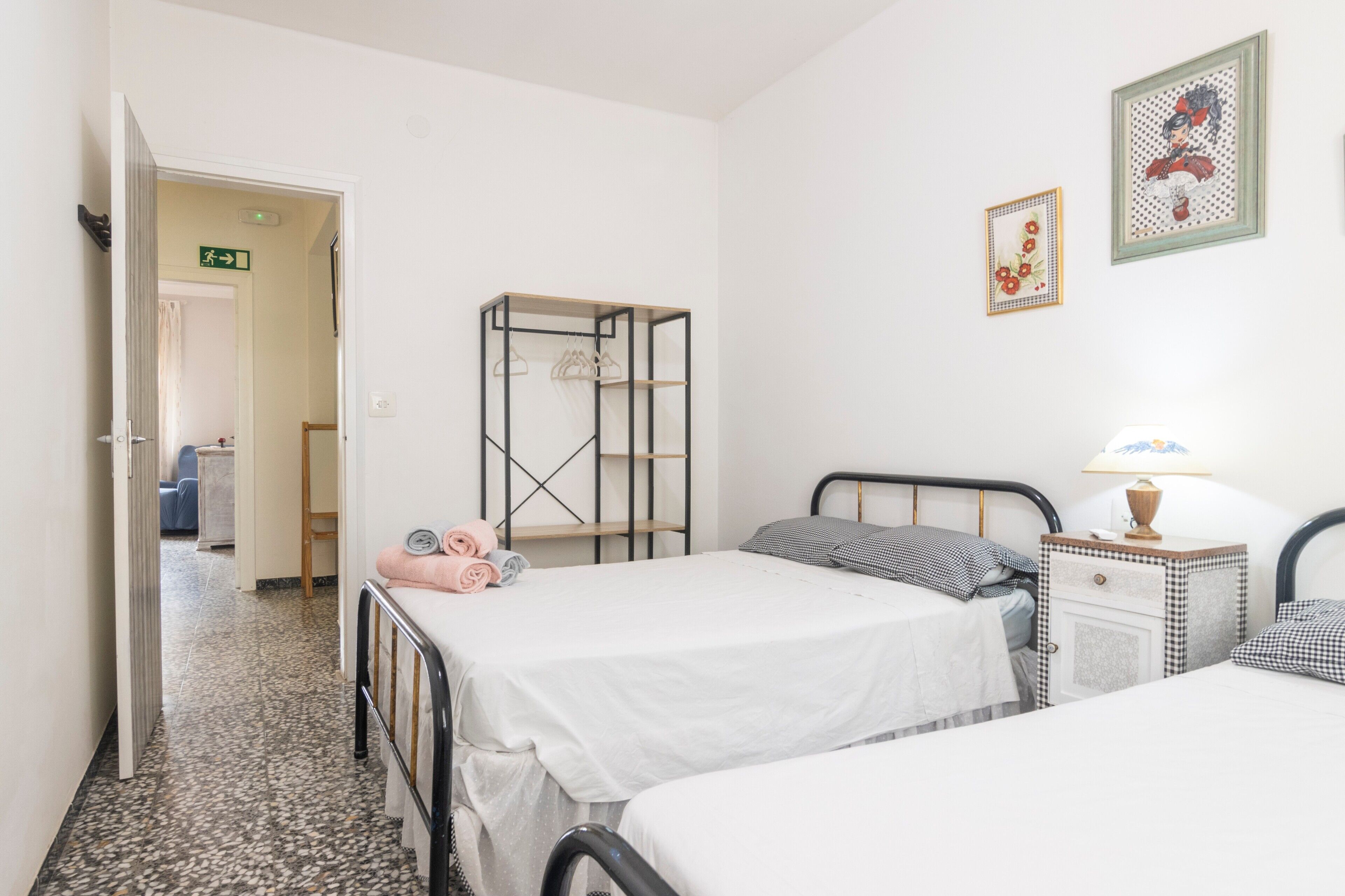 Habitació d'hotel amb dos llits, una taula de nit amb una làmpada, un armari i un quadre al mur.