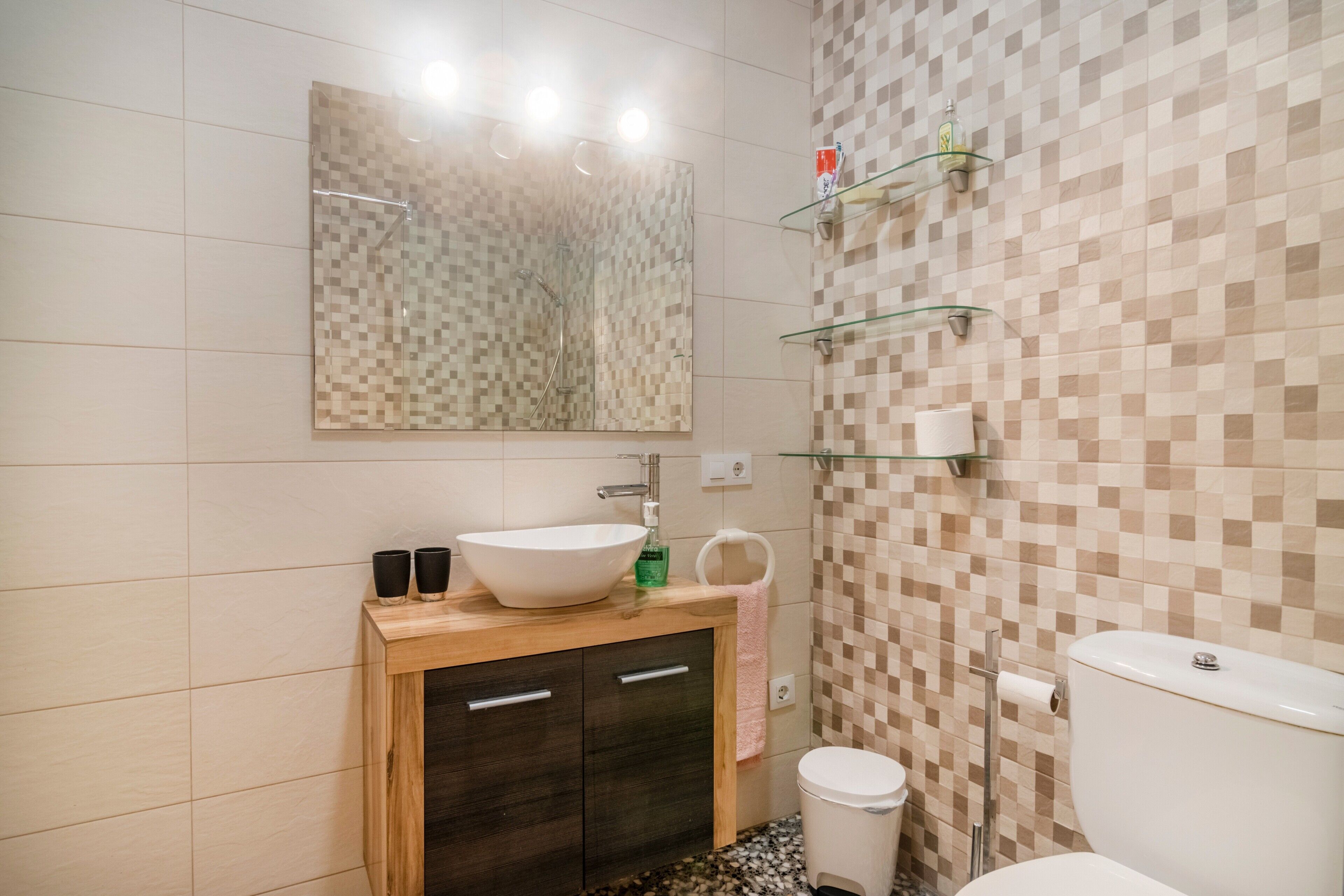 Ein Badezimmer mit einem Holzkosmetikschrank, einem großen Spiegel, einem weißen Waschbecken und einer Toilette.