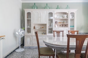 A dining area with a round table, chairs, a fan, and a cabinet with glass doors.