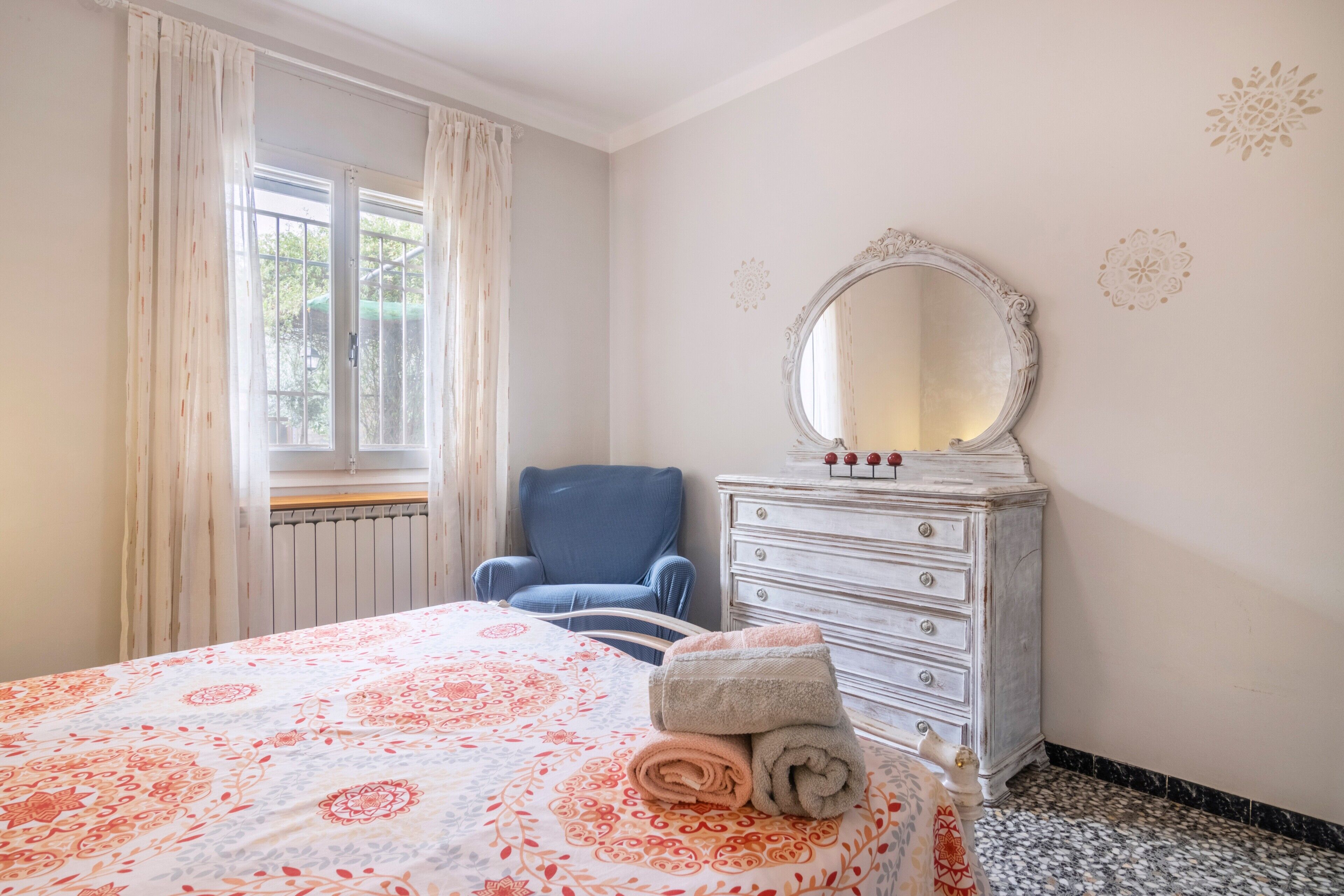 Ein Schlafzimmer mit Bett, Kommode, Stuhl und einem Fenster mit Vorhängen.