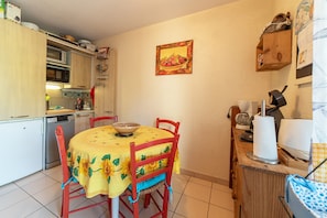 A compact kitchen with a dining table, chairs, a microwave, and a coffee maker. - Holiday Home 'Maison Marina Au Bacarès' with Private Terrace, Private Garden and Wi-Fi (Le Barcarès)