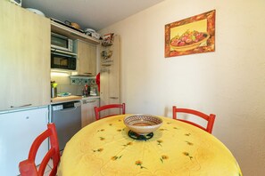 A compact kitchen with a microwave, oven, and dishwasher. A dining table with a floral tablecloth and a bowl is centered.