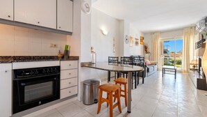 Una cocina moderna con horno empotrado, un comedor con mesa y sillas redondas, y vistas al exterior a través de amplios ventanales.