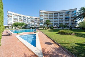 A hotel with a swimming pool, multiple balconies, and a well-maintained lawn.