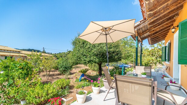 Eine Terrasse mit Tisch, Stühlen und Sonnenschirm. Kübelpflanzen und Blick auf einen Garten.