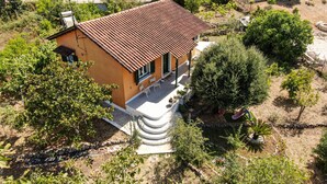 Ein eingeschossiges Haus mit Ziegeldach, umgeben von viel Grün und einem kleinen Garten.