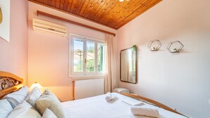 Ein Schlafzimmer mit Holzboden, einem Fenster mit Vorhängen, einem Bett mit weißen Leinen und einem wandmontierten Spiegel.