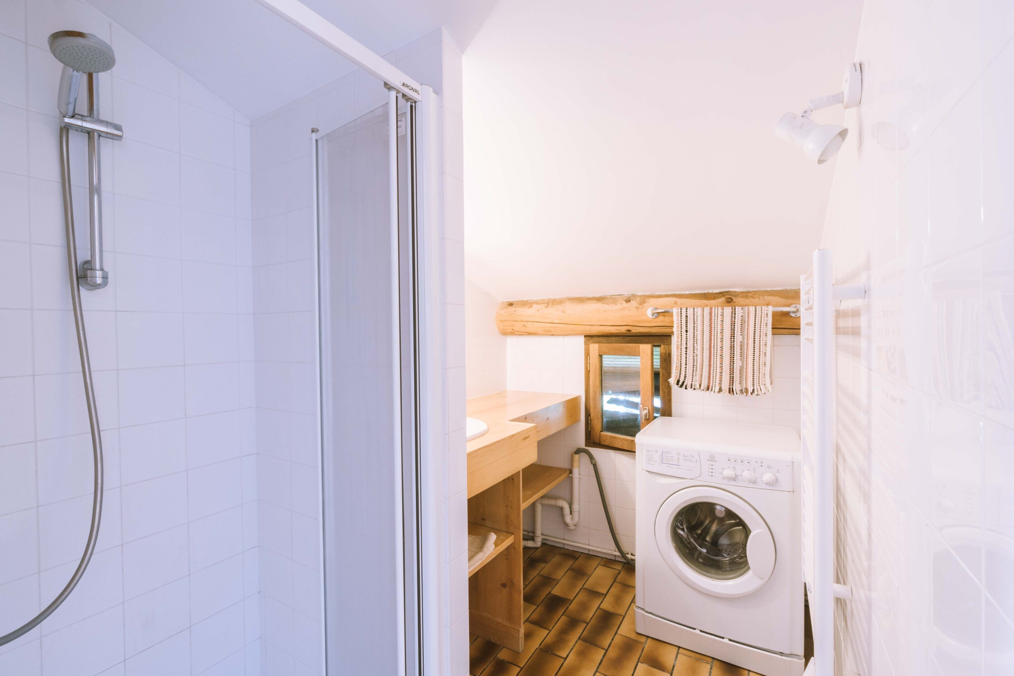 Une petite salle de bain comprenant une douche, un lavabo, un lave-linge et une étagère en bois.