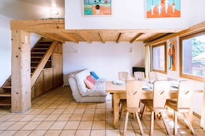 Una habitación con una escalera de madera, un sofá con cojines, una mesa de comedor con sillas y obras de arte en las paredes.