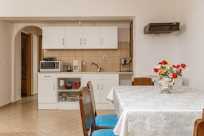 A compact kitchen with white cabinets, a microwave, a coffee maker, and a sink. There's a dining table with a white tablecloth and a vase with flowers.