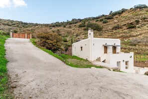 A white building with a sloped roof, a small porch, and a paved road leading to a gate.