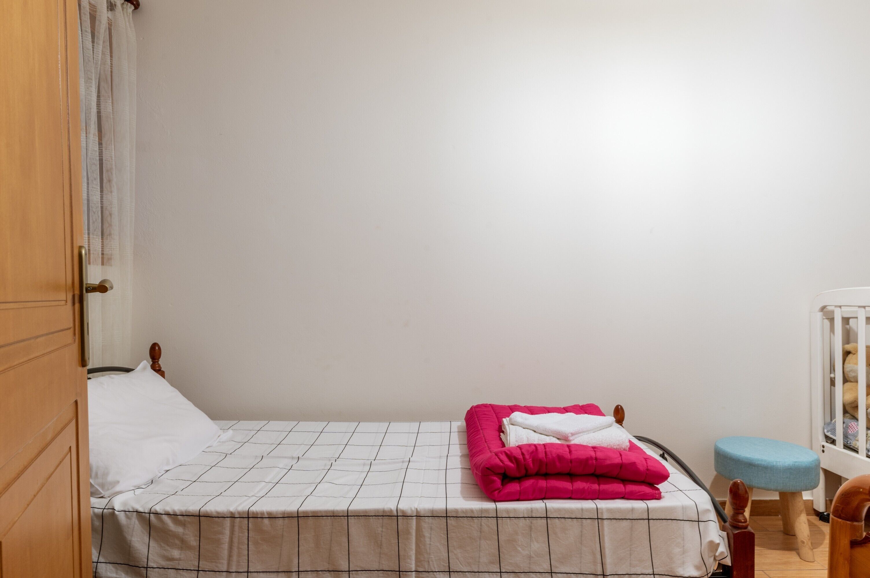 Una cama individual con una colcha blanco y negra a cuadros, una manta rosa y una almohada blanca.