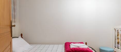 Una cama individual con una colcha blanco y negra a cuadros, una manta rosa y una almohada blanca.