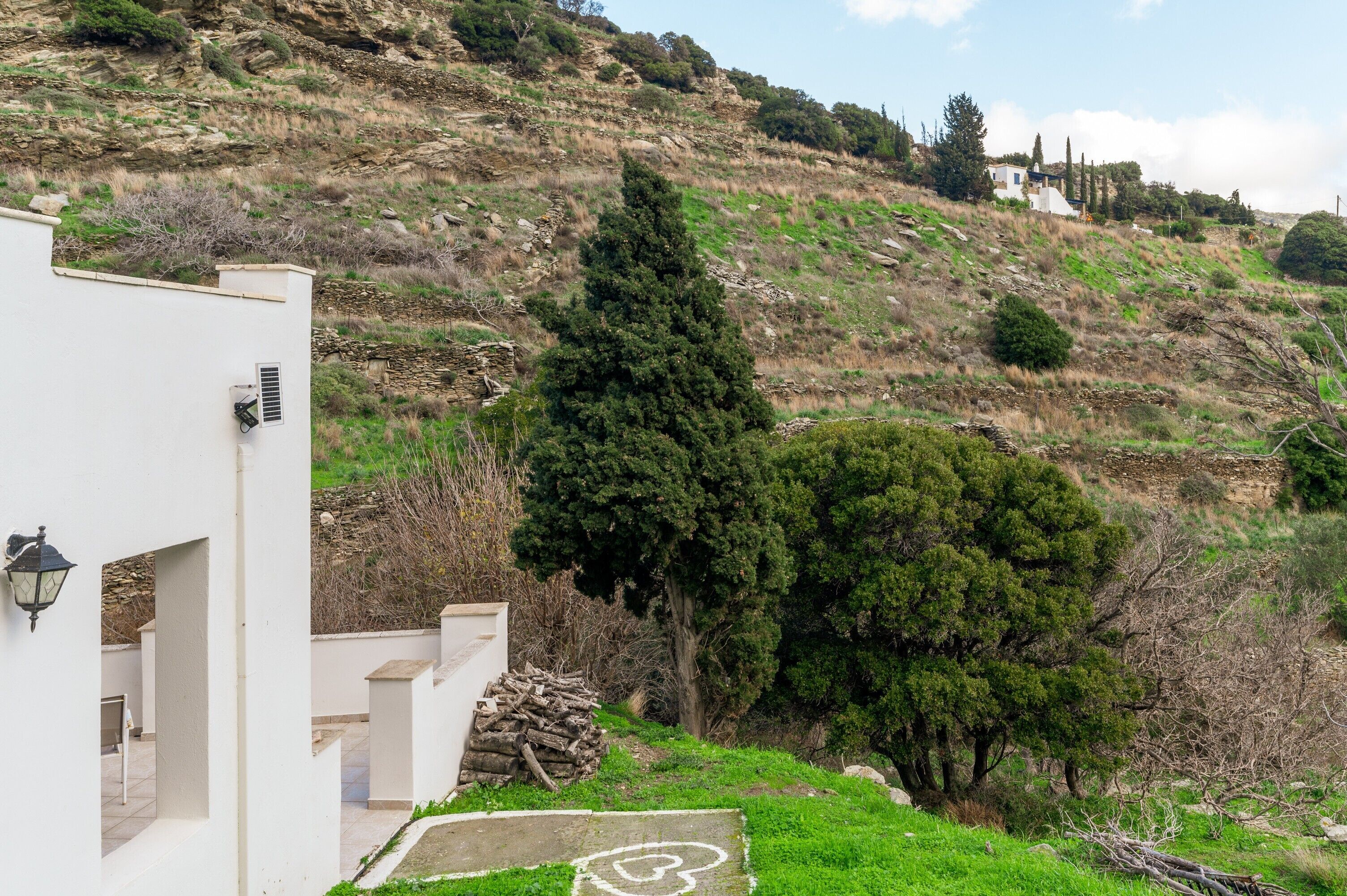 Un pendio con un edificio bianco, un albero grande e un paesaggio roccioso.