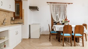 Une cuisine équipée d’un réfrigérateur, d’un évier et d’une fenêtre avec un rideau. On y trouve une table à manger avec des chaises et un vase rempli de fleurs.