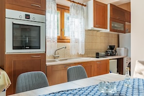 Una cocina con armarios de madera, horno empotrado, lavabo y una mesa de comedor con sillas.
