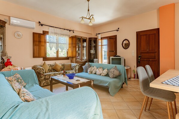 Una sala de estar con dos sofás, una mesa de centro, un televisor y una mesa de comedor con sillas.