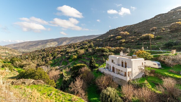 Ein modernes Haus mit weißer Fassade, umgeben von üppiger Vegetation und Hügeln im Hintergrund.