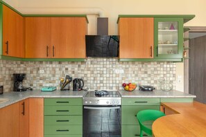 A kitchen with green cabinets, a tiled backsplash, and a stove.