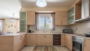 A modern kitchen with wooden cabinets, a built-in microwave, an oven, a window with curtains, and a tiled floor. - Holiday Home 'Villa Melenia 1' with Private Pool, 5 Minutes from the Beach, Wi-Fi & Air Conditioning (??. ?e?a??a)