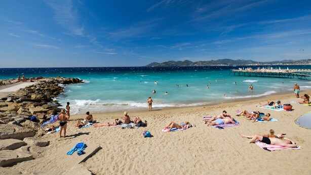 A beach with people sunbathing and swimming, a pier extending into the water, and a clear blue sky. - Apartment "T2 a 50 m Plage du Midi" with Shared Terrace & Wi-Fi (Cannes)