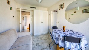 A room with a sofa, a dining table with a patterned tablecloth, a mirror, and a door leading to another room. - Apartment "T2 a 50 m Plage du Midi" with Shared Terrace & Wi-Fi (Cannes)