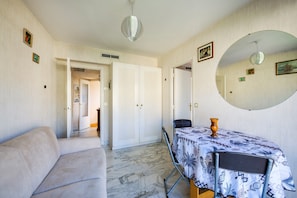 Ein Zimmer mit einer Couch, einem Esstisch mit gemustertem Tischläufer, einem Spiegel und einer Tür zu einem anderen Raum.