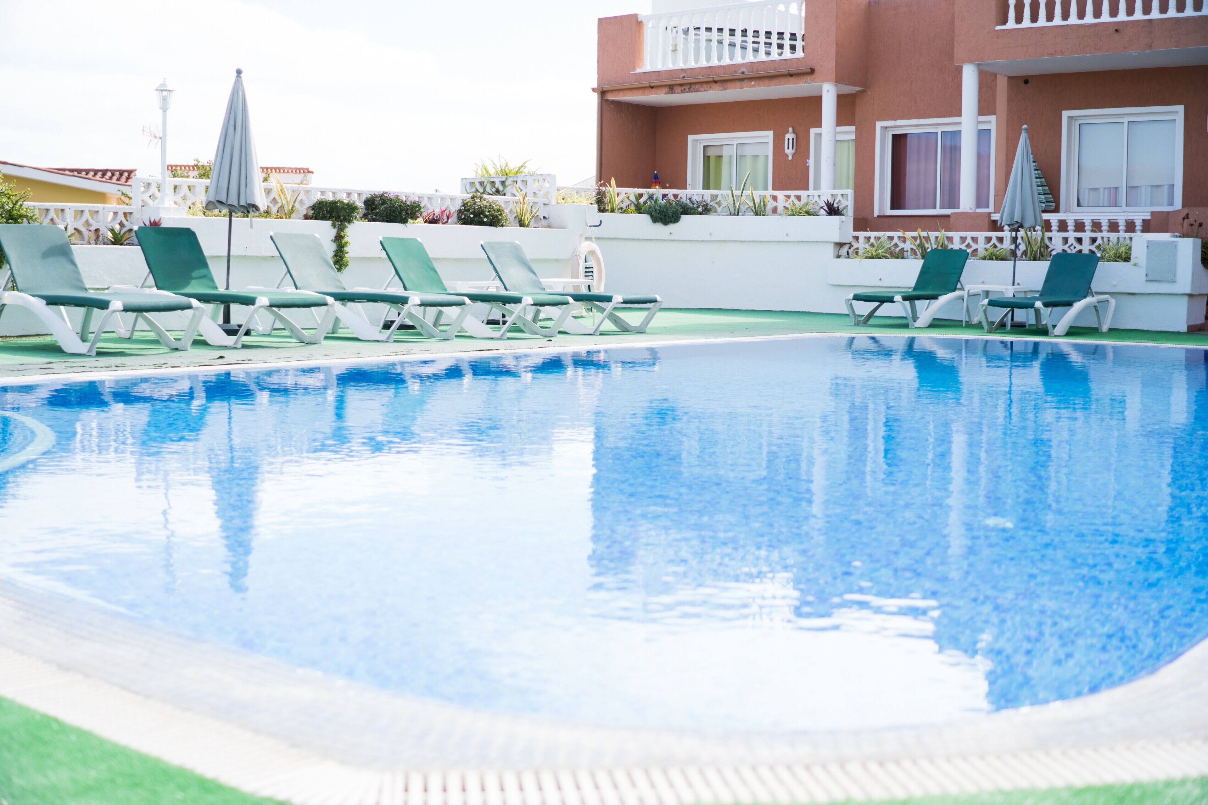 Une piscine entourée d’un bâtiment doté de balcons, avec des chaises longues et des parasols à proximité.