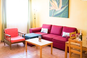 Un salon avec un canapé rouge, une chaise en bois, une petite table et un lampadaire.