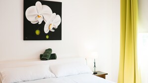 Una habitación de hotel con una cama, una toalla verde, una mesita de noche, una lámpara y un cuadro de flores blancas.